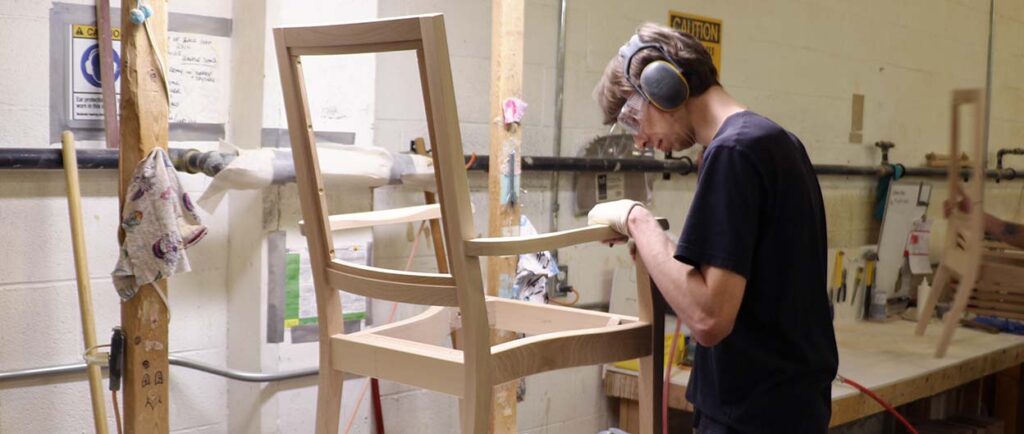 Produktionsmitarbeiter beim Schleifen eines hölzernen Stuhlrahmens